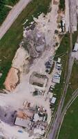 Construction zone in the fields near the railways. Materials for construction and machines scattered by the site. Top view. Forest at the backdrop. Vertical video