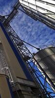 moderno grande granaio a luce del sole. agricolo produzione. agricoltura grano silos Conservazione cisterna. grande metallo silos su blu cielo sfondo. verticale video