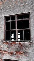 Forlorn building with crashed windows. Approaching to the brick wall of the construction. Industrial chimney pipe at the backdrop. Vertical video