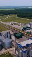 moderno tecnologico pianta per Conservazione e in lavorazione grano raccolti. ben tenuto industriale territorio diviso di linee ferroviarie con carico treni. bellissimo natura paesaggio sfondo. verticale video