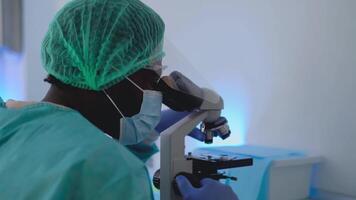 un persona en un laboratorio Saco mirando mediante un microscopio video