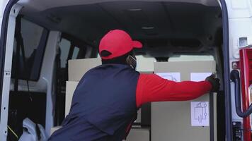 en man i en röd hatt och röd väst är läser in lådor in i en skåpbil video