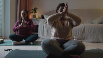 two women are sitting on yoga mats in a living room video