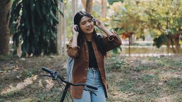 estilo de vida, educación, adolescencia. Adolescente estudiante en auriculares con teléfono inteligente bicicleta sentado en parque, hembra mira a teléfono pantalla video