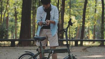 estilo de vida, educación, adolescencia. Adolescente estudiante en auriculares con teléfono inteligente bicicleta sentado en parque, hembra mira a teléfono pantalla video