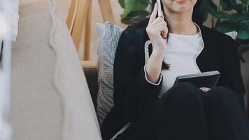 Asian working woman wearing black shirt and writing journal on small notebook on the table at indoor cafe. Woman notes and drinking coffee at cafe. Working from anywhere concept. video