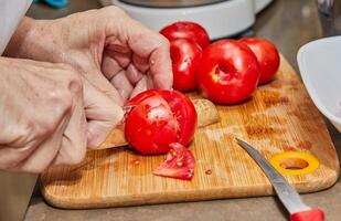 Chef's Hands Cutting Fresh Tomatoes on Wooden Cutting Board in Kitchen photo