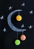 Chalk drawing of a crescent moon with macarons hanging from it photo