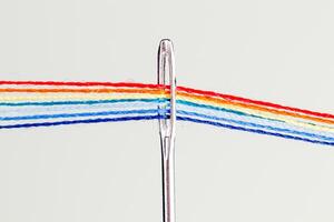 multi-colored threads for sewing in the form of a rainbow pass through an antique needle on a white background photo