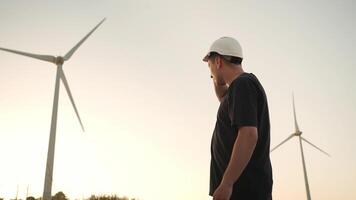 een Mens in een moeilijk hoed staand in voorkant van een wind turbine buitenshuis video