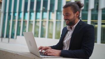 a man in a suit is leaning on a wall and using his laptop video