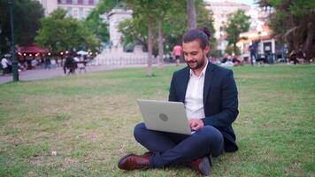 uma homem dentro uma terno é sentado em a parque com dele computador portátil video