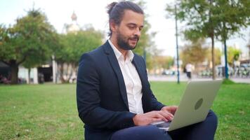 une homme dans une costume est séance dans une parc avec le sien portable video