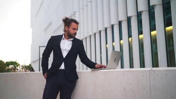 un hombre en un traje es propensión en contra un pared con su ordenador portátil video