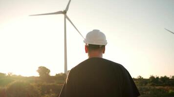 un hombre en un difícil sombrero en pie en frente de un viento turbina al aire libre video