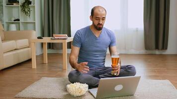 Mann mit Bier und Popcorn auf Video Anruf reden mit freunde während covid Einschränkungen.