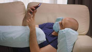 Man with protection mask during coronavirus lockdown scrolling on smartphone while hugging a pillow. video