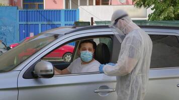 uomo dà un' test per coronavirus nel il suo automobile attraverso il finestra. video