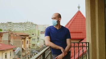 Deprimido hombre con proteccion máscara en el terraza durante coronavirus pandemia. video