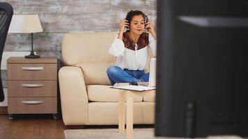 vrouw gebruik makend van hoofdtelefoons gedurende een video telefoontje terwijl werken van huis zittend Aan bankstel in leven kamer.