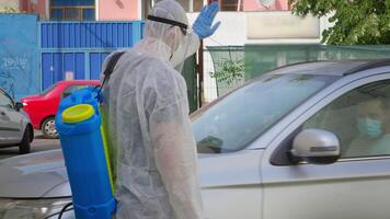 hombre en bata pulverización coche con saneamientos solución en contra COVID-19. video