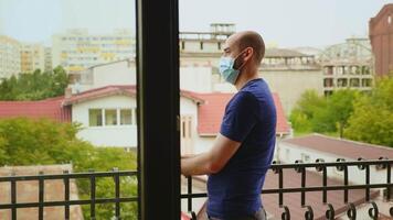 glücklich Mann mit medizinisch Maske auf Balkon während Coronavirus Pandemie selbst Isolierung video