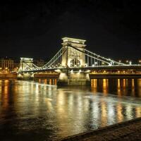 ai generado antiguo hierro puente a noche en el ligero de luces de la calle a través de el Danubio río en Budapest Hungría foto