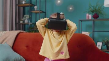 Toddler girl sitting on home sofa using virtual reality headset helmet app to play simulation game video