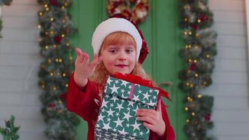 Happy toddler child girl kid in red sweater presenting one Christmas gift box, stretches out hands video