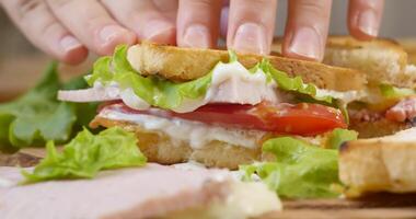 groß appetitlich Sandwich mit Schinken, reif Tomate Scheiben und Stücke von Käse, Grüner Salat und Mayonnaise Soße. schnell Essen Konzept. Ultra 4k video