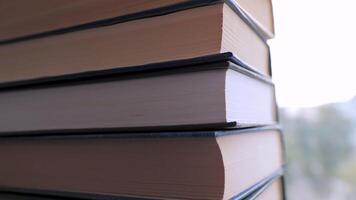 Close-up of a Stack of Colorful Old Hardcover Books in Rays of Sunlight. Camera movement from the bottom. Home collection of books on blurred background. Concept of learning, reading, and knowledge. video