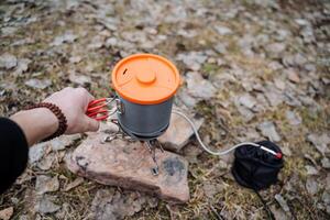 Tourist utensils stand on the stones, cook food on a hike in the camp, hand holds a pot of water, photo