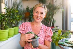 Happy woman gardening on balcony at home. She is showing growth of her houseleek plant photo