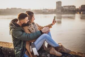 Happy couple photographing  cityscape with mobile phone  while spending time together by the river. photo