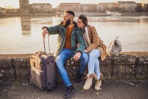 preocupado Pareja turistas tiene perdido en su vacaciones y ahora ellos son confuso cuales camino a Vamos mientras sentado por el río con su equipaje. foto