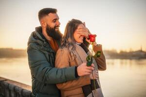 contento hombre dando rojo Rosa a su mujer mientras ellos disfrutar gasto hora juntos en un puesta de sol. foto