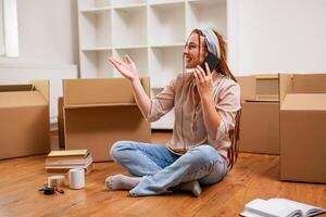 Modern ginger woman with braids talking on the phone while moving into her new apartment. photo