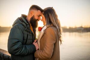 Happy man giving red rose to his woman while they enjoy spending time together on a sunset. photo