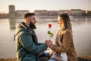 hombre dando rojo Rosa a su mujer mientras ellos disfrutar gasto hora juntos exterior. foto