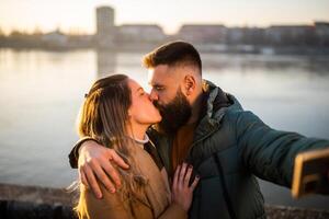 cerca arriba imagen de contento Pareja tomando selfie mientras besos exterior. foto