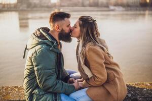 Happy couple kissing and holding hands while  enjoy sitting by the river. photo