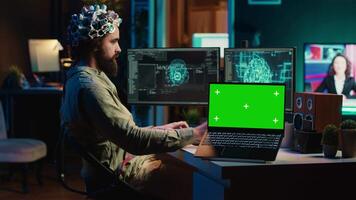 Ingenieur mit eeg Headset auf Programmierung Gehirn Transfer in Computer virtuell Welt Nächster zu Grün Bildschirm Laptop. transhumanistisch mit Neurowissenschaften zu dazugewinnen Digital Seele, Attrappe, Lehrmodell, Simulation Gerät, Kamera ein video