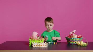 Joyful small kid painting eggs for easter holiday festivity in studio, using watercolor and art supplies. Smiling preschooler coloring festive ornaments in preparation for sunday. Camera B. video