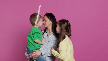 Adorable lovely family showing love and laughing on camera, children feeling happy and playful in studio. Mother with a boy and a girl kissing and hugging each other, joyful people. Camera A. video