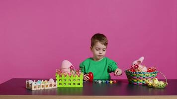 Small sweet child decorating eggs with stamps and watercolor, preparation for easter sunday holiday. Joyful little boy having fun coloring festive decorations, painting designs in studio. Camera B. video