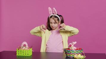 Displeased unhappy child giving thumbs down in studio, expressing her disapproval and disagreement with dislike symbol. Angry dissatisfied young girl showing negative bad gesture. Camera A. video