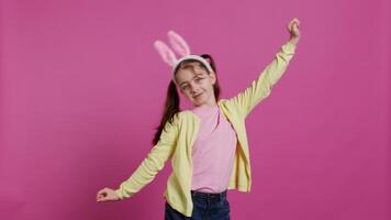 confidente alegre niña demostración danza se mueve en el estudio, sensación alegre y positivo acerca de Pascua de Resurrección fiesta festividad. talentoso niño bailando alrededor y vistiendo conejito orejas. cámara b. video