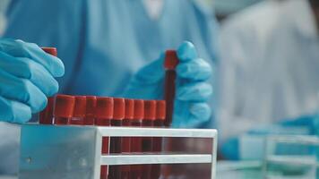 médico mano tomando un sangre muestra tubo desde un estante con máquinas de análisis en el laboratorio fondo, técnico participación sangre tubo prueba en el investigación laboratorio. video