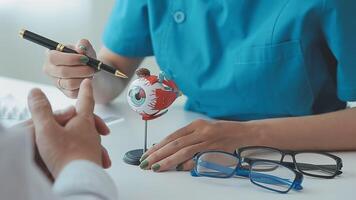 proche en haut de asiatique femelle médecin portant visage masque est montrant globe oculaire modèle et expliquant à propos yeux maladie à aîné Sénior homme patient dans hôpital video