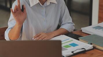 mujer de negocios asiática que usa una computadora portátil y trabaja en la oficina con un documento de calculadora en el escritorio, planificando el análisis del informe financiero, la inversión del plan de negocios, el concepto de análisis financiero. video